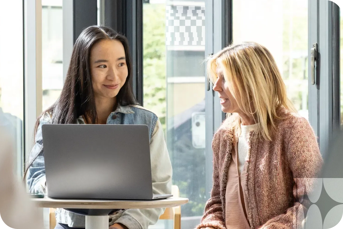 Two people talk while looking at a laptop.
