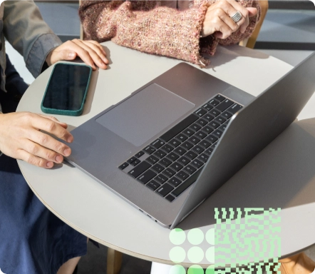 A photo of a laptop and a phone on a table with two pairs of hands.